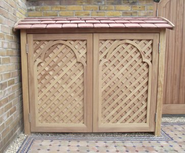 Wooden lattice storage unit with a sloped roof against a brick wall.