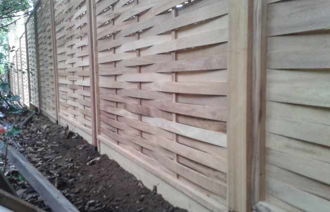 Wooden slat fence with soil and leaves along its base.