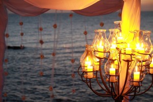 Lit chandelier under a canopy by the sea at sunset.