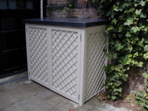 White lattice storage box with a black lid, placed outdoors near a brick wall and ivy.