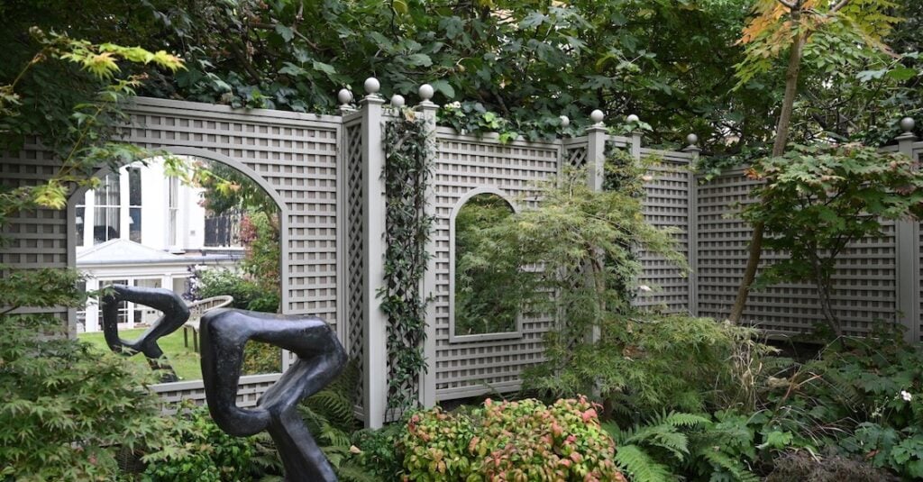 Garden with a lattice fence, abstract sculpture, and lush greenery.