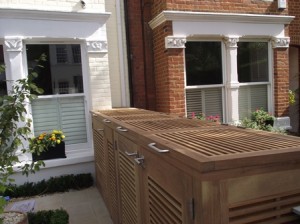 Wooden slatted outdoor storage unit next to brick and white-painted buildings with windows.