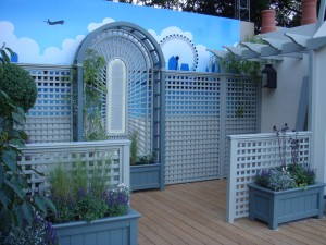 Garden patio with wooden lattice walls and planters, decorative arch, and a mural with a city skyline and plane.