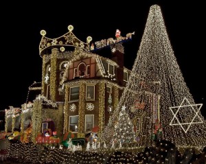 House adorned with extensive holiday lights and decorations, featuring a large illuminated tree and star.