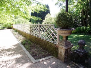 Garden path with trellis fence, potted tree, stone decor, and lush greenery in the background.