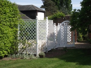 White lattice gate and fence in a garden area with greenery and trees.
