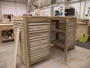 Wooden slatted cabinet with open shelving in a workshop setting.