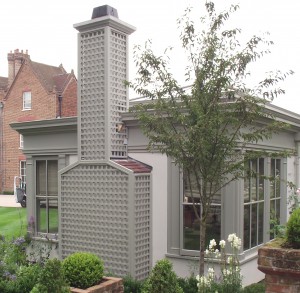Modern house with large windows, a tall lattice chimney, and a small tree in the garden.