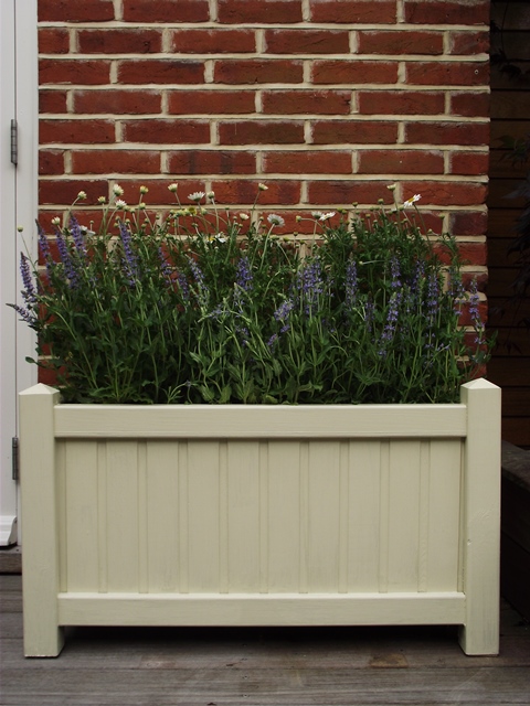 A wooden planter box with lavender plants against a brick wall.