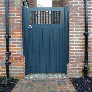 A tall, gray wooden gate with vertical slats is set between two brick walls, with black drainpipes on each side.