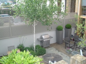 Modern backyard with a grill, seating area, potted plants, and a lattice fence.