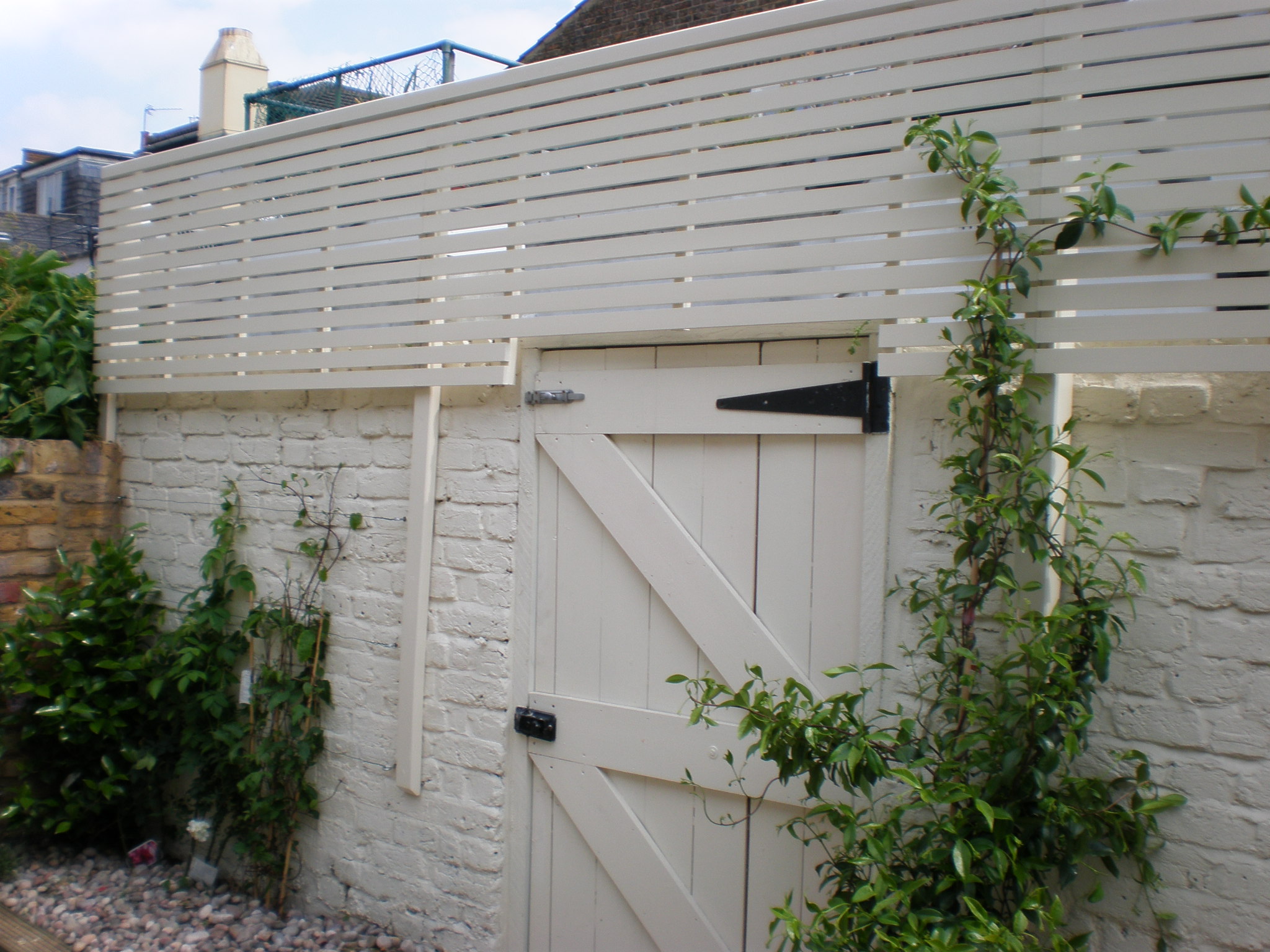White wooden gate and fence with climbing plants, set against a white brick wall.