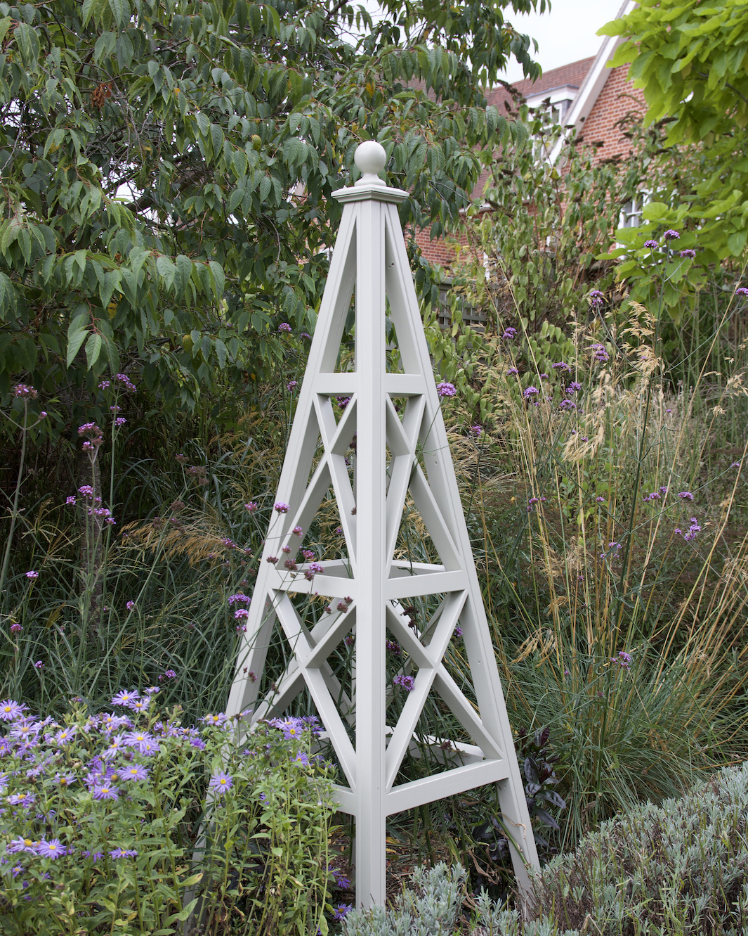 A wooden garden obelisk surrounded by various plants and flowers in a garden.