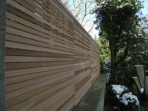 A wooden slatted fence beside a snow-dusted garden area with trees in the background.