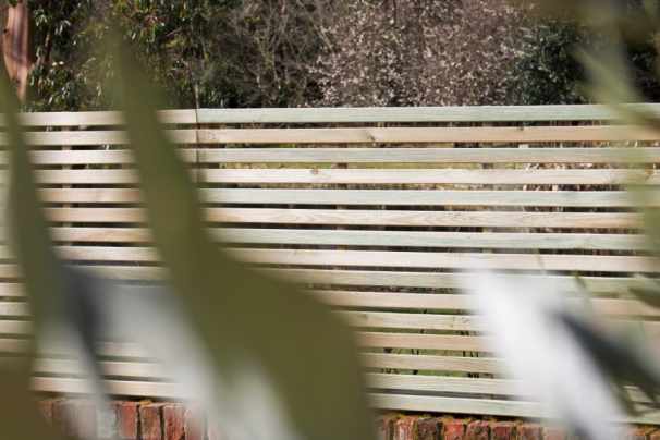 Slatted wooden fence with foliage partially obscuring the view.