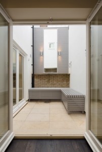 Open double doors leading to a small courtyard with a bench, surrounded by white walls and shuttered windows.
