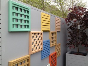 Colorful lattice panels mounted on a gray wall, next to a potted tree with red foliage.