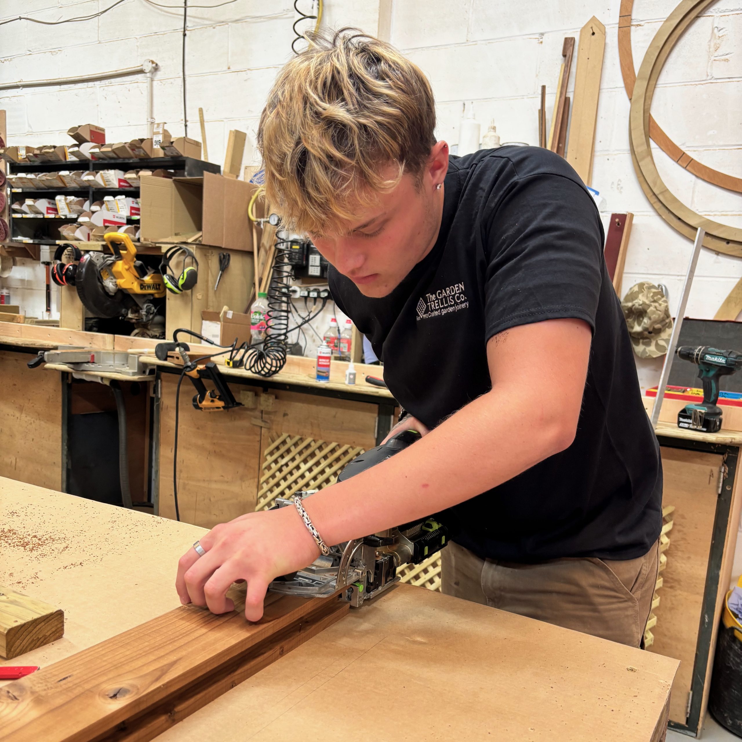 A man wearing a black Garden Trellis Co t-shirt doing wood work